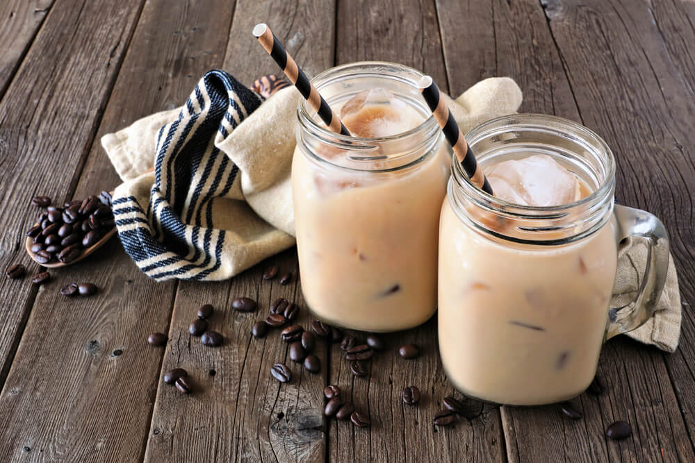 Ľadové kávové smoothie v dvoch pohároch so slamkami a pohádzanými zrniečkami kávy na drevenom pozadí